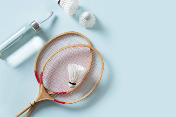 Two badminton rackets, shuttlecock, and a sports bottle on a light blue surface.